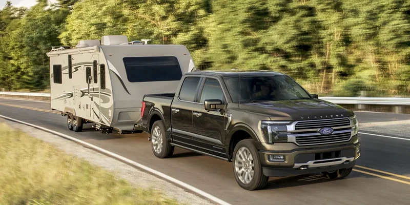 Black 2025 Ford F-150 towing a camper on a forested road